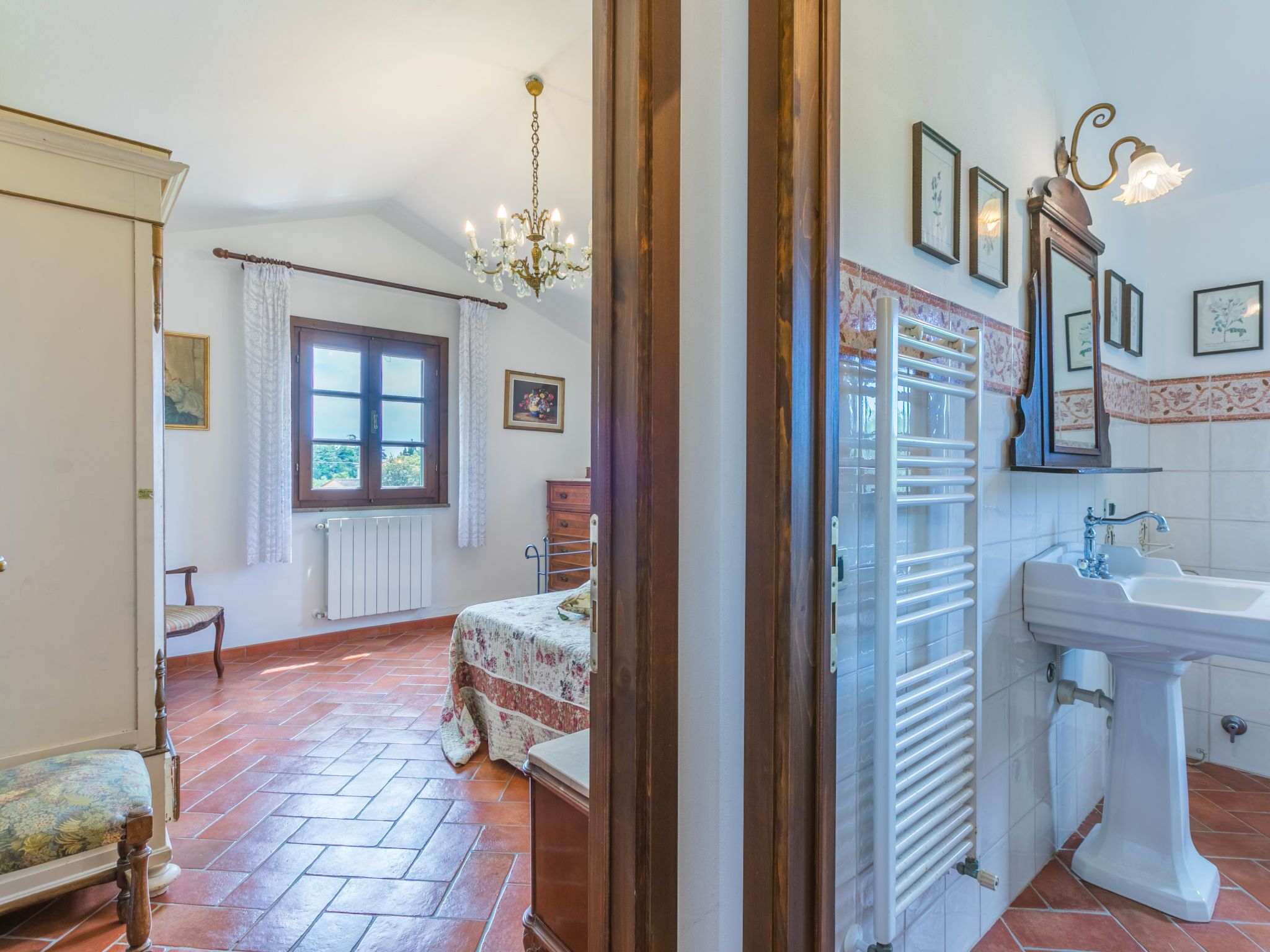 A bedroom with a bed, a window, a radiator, a wooden chair, and a chandelier.