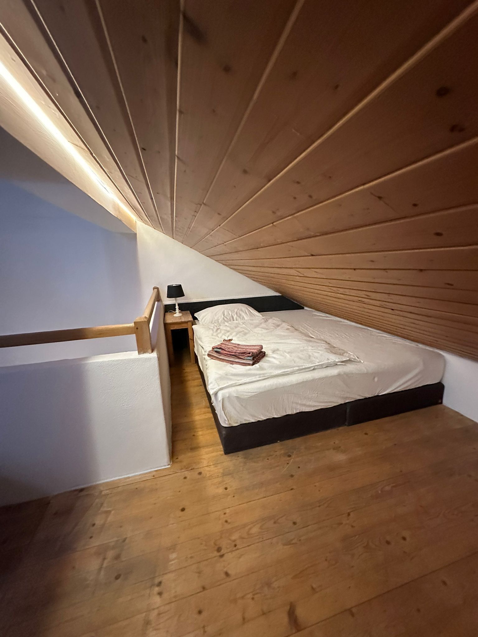 A small, single-bed room with wooden slats on the ceiling and a wooden floor.