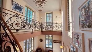 A spacious interior with a high ceiling, ornate iron railing, large windows, and multiple framed artworks. - L'Isle sur la Sorgue, country house (Le Thor)