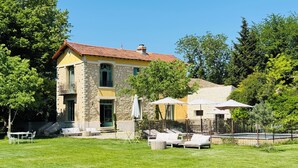 A two-story stone building with a red-tiled roof, a balcony, and a grassy yard with outdoor seating. - L'Isle sur la Sorgue, country house (Le Thor)