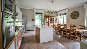 A kitchen with stainless steel appliances, a central island, wooden chairs, and a dining table.
