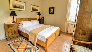 A bedroom with a wooden bed, two bedside tables, a nightstand, a patterned rug, and two framed pictures on the wall.