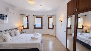 A bedroom with a bed, bedside tables, a mirror, and windows with curtains. - Villa Noa Amazing Sea view (Kas)