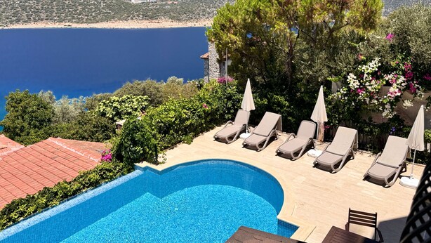 A pool with lounge chairs, a stone wall, and a view of the sea and mountains. - Villa Noa Amazing Sea view (Kas)