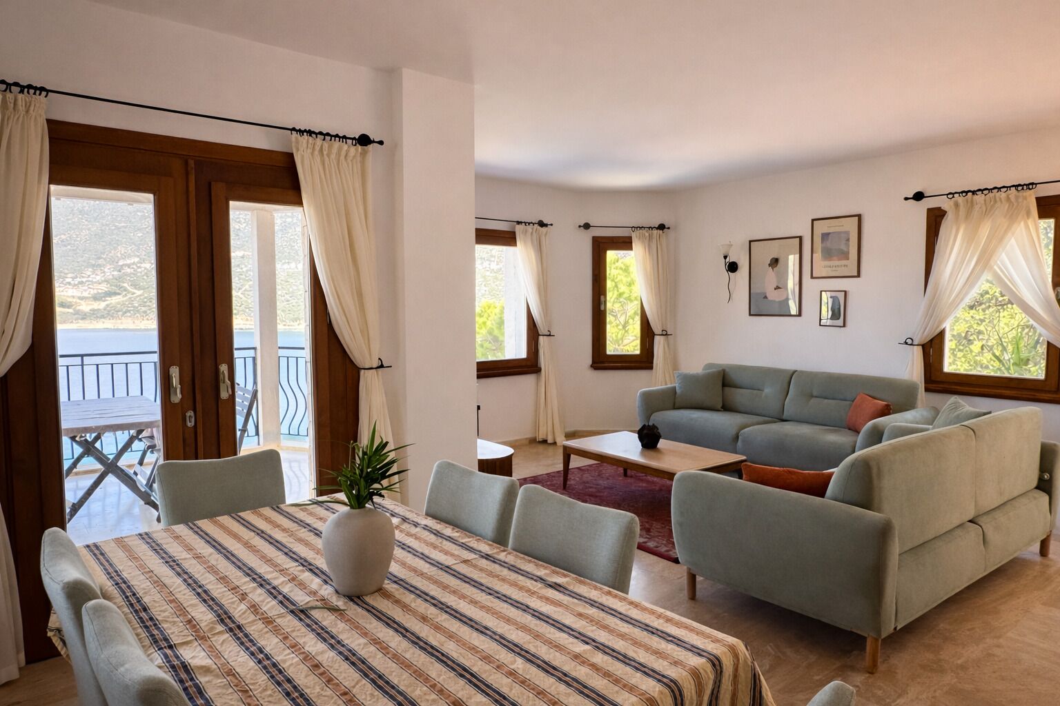 Una sala de estar con un sofá, una mesa de comedor con sillas y vistas al exterior a través de grandes ventanales.