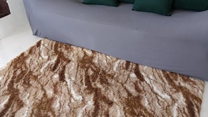 Een bank met groene kussens en een vloerkleed met bruin-wit patroon.