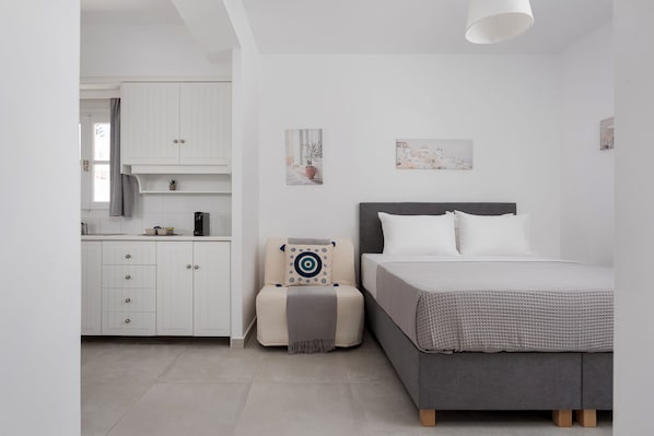 Un dormitorio moderno con cama, mesita de noche y una pequeña zona de estar con cojín y almohada.
