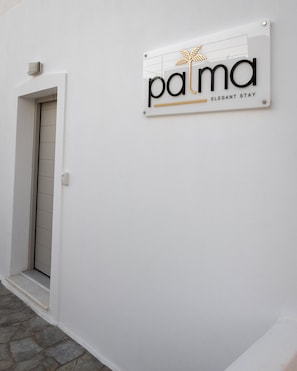 A sign with the word 'palma' and 'elegant stay' on a white wall. - Palma Elegant Suites (Naousa)