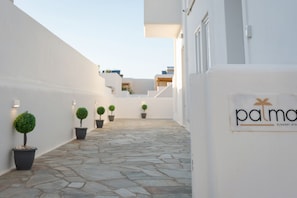 A narrow stone-paved corridor with white walls, potted plants, and a sign reading 'palma' with a palm tree logo. - Palma Elegant Suites (Naousa)