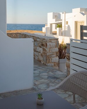 A balcony with a view of the sea, stone walls, a small potted plant, and a wicker chair. - Palma Elegant Suites (Naousa)
