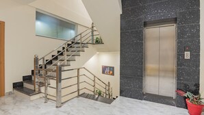 A modern interior with a marble staircase, a wall-mounted artwork, and a marble elevator. - Treebo Gaur Vasundhara (Vrindavan)