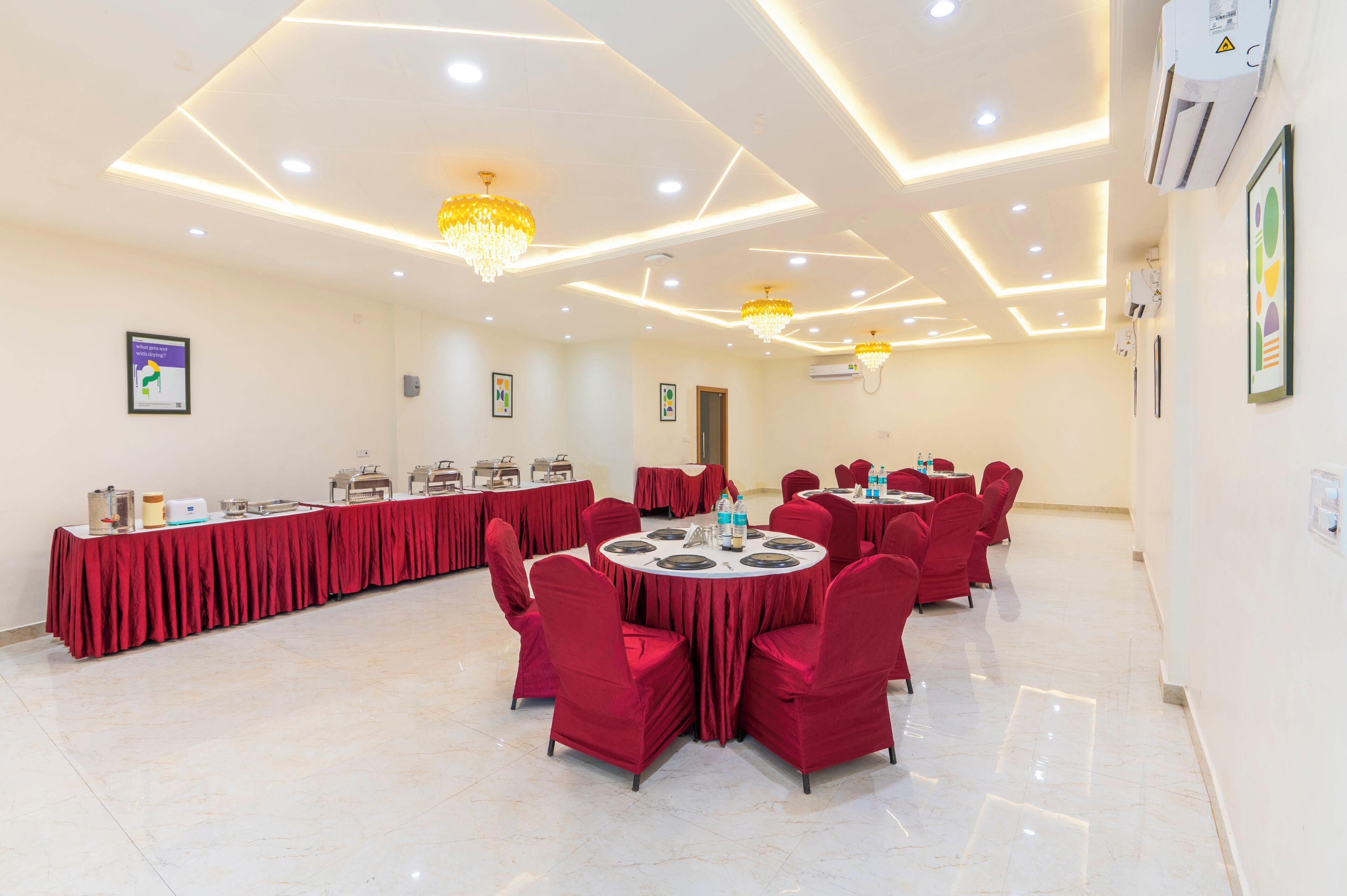 A conference room with round tables, red chairs, and a long table with food and drinks.