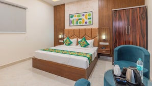 A hotel room with a bed, a desk with a chair, a wardrobe, and a painting on the wall. - Treebo Gaur Vasundhara (Vrindavan)