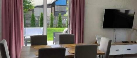 Un comedor moderno con una mesa, sillas, un televisor de pantalla plana y vistas a un jardín.