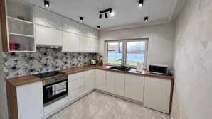 A modern kitchen with white cabinets, a wooden countertop, and a large window providing a view of the outdoors. - Apartamenty Max House (Zator)
