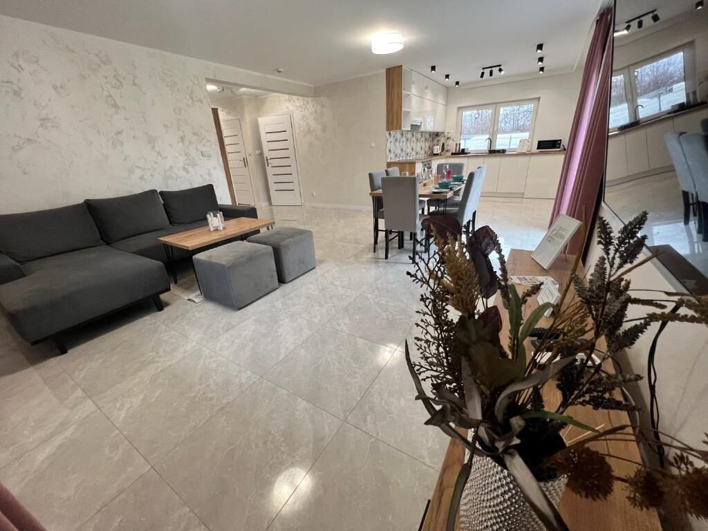 Un salon moderne avec un canapé d’angle gris, une table basse en bois et une plante décorative.
