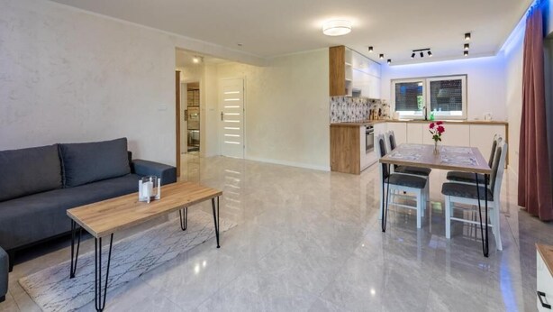 A modern living room with a sofa, coffee table, and dining area with chairs and a table. - Apartamenty Max House (Zator)