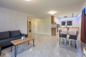 A modern living room with a sofa, coffee table, and dining area with chairs and a table. - Apartamenty Max House (Zator)