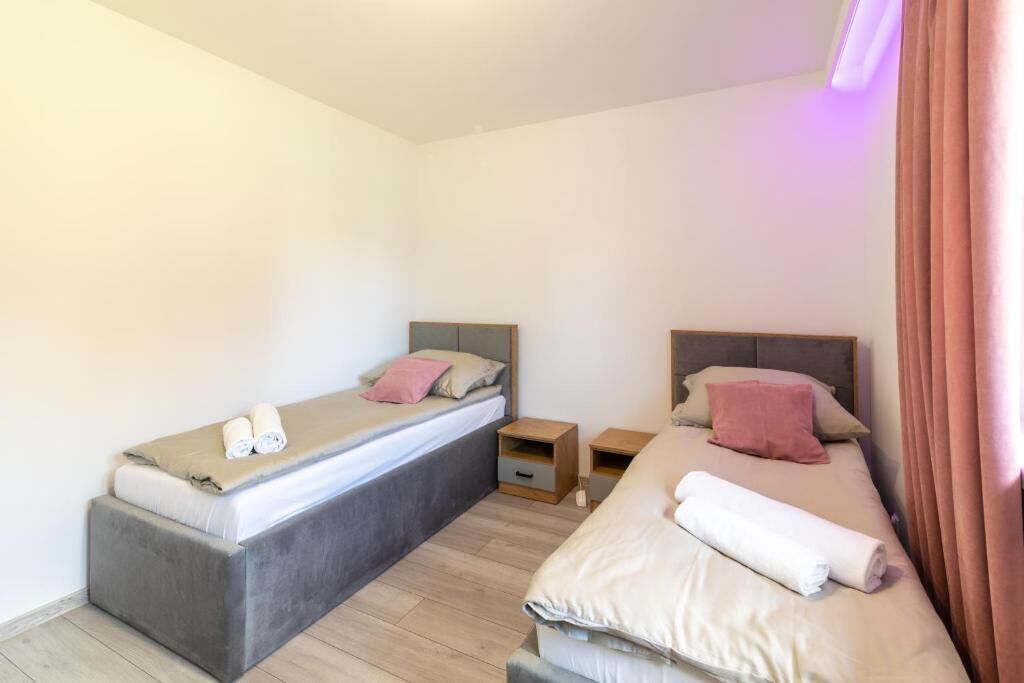 Una camera da letto piccola e moderna con due letti, ognuno con un cuscino e un asciugamano arrotolato. Ci sono due comodini, uno tra ogni letto.