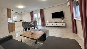A modern living room with a sofa, a dining table, and a TV. - Apartamenty Max House (Zator)