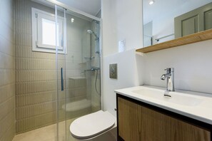 A modern bathroom with a glass-enclosed shower, a white toilet, and a wooden vanity with a sink. - Phaedrus Living: Paros Cycladic Residences 8 (Paros)