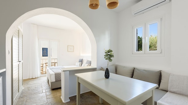 A bright, airy room with a white table, a sofa, and a large window. - Phaedrus Living: Paros Cycladic Residences 8 (Paros)