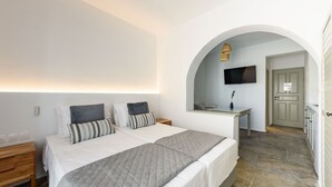 A bedroom with a large bed, a bedside table, a TV mounted on an arched wall, and a small desk with a chair. - Phaedrus Living: Paros Cycladic Residences 8 (Paros)