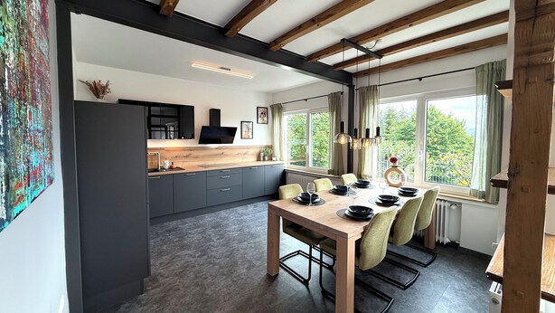 A modern kitchen with dark cabinets, a wooden countertop, and a dining area with a table set for four.