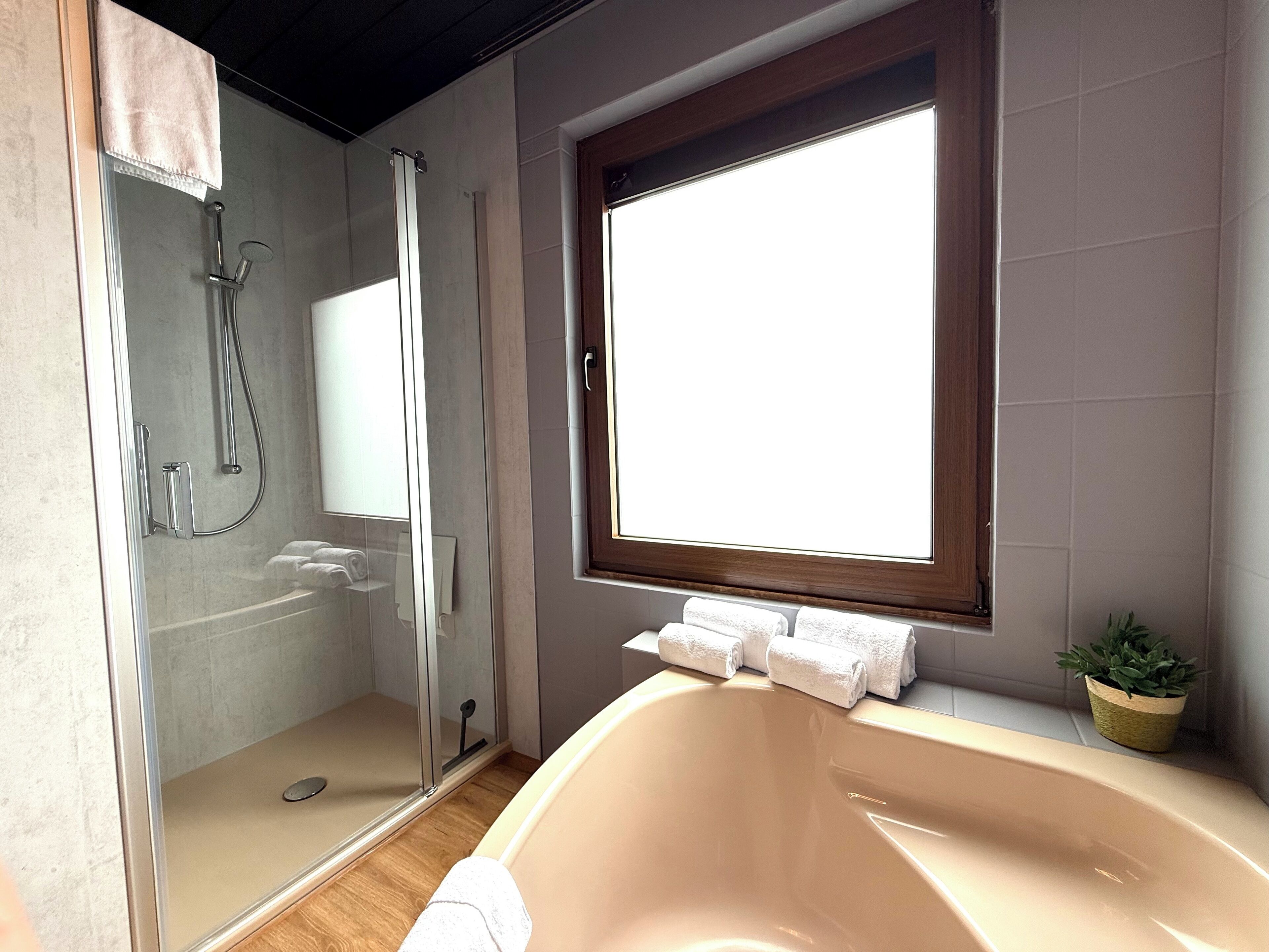 A bathroom with a glass-enclosed shower, a bathtub, and a window providing natural light.