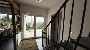 A modern interior with a staircase, a dining area with chairs and a table, and a view through the glass doors.