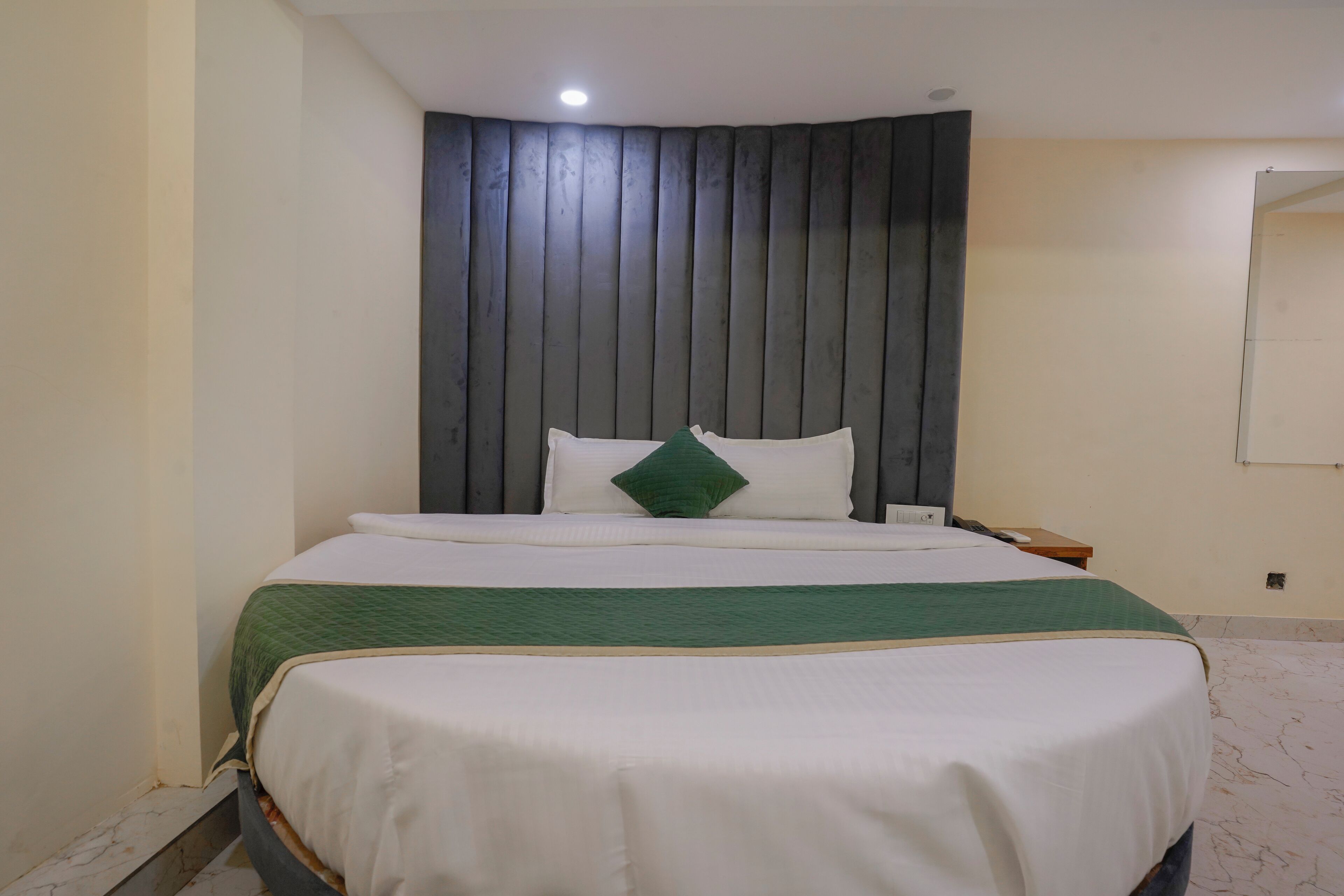 A neatly made bed with a green and white bedspread, a wooden headboard, and a small bedside table with a lamp.