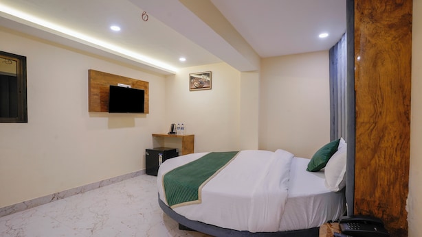 A hotel room with a bed, a television mounted on the wall, a small table with a remote control, and a wooden accent wall. - Crystal By Glitz Hotels (Mumbai)