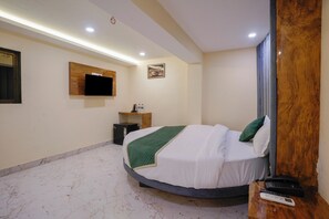Habitación de hotel con una cama, un televisor montado en la pared, una mesita con un control remoto y una pared decorativa de madera.