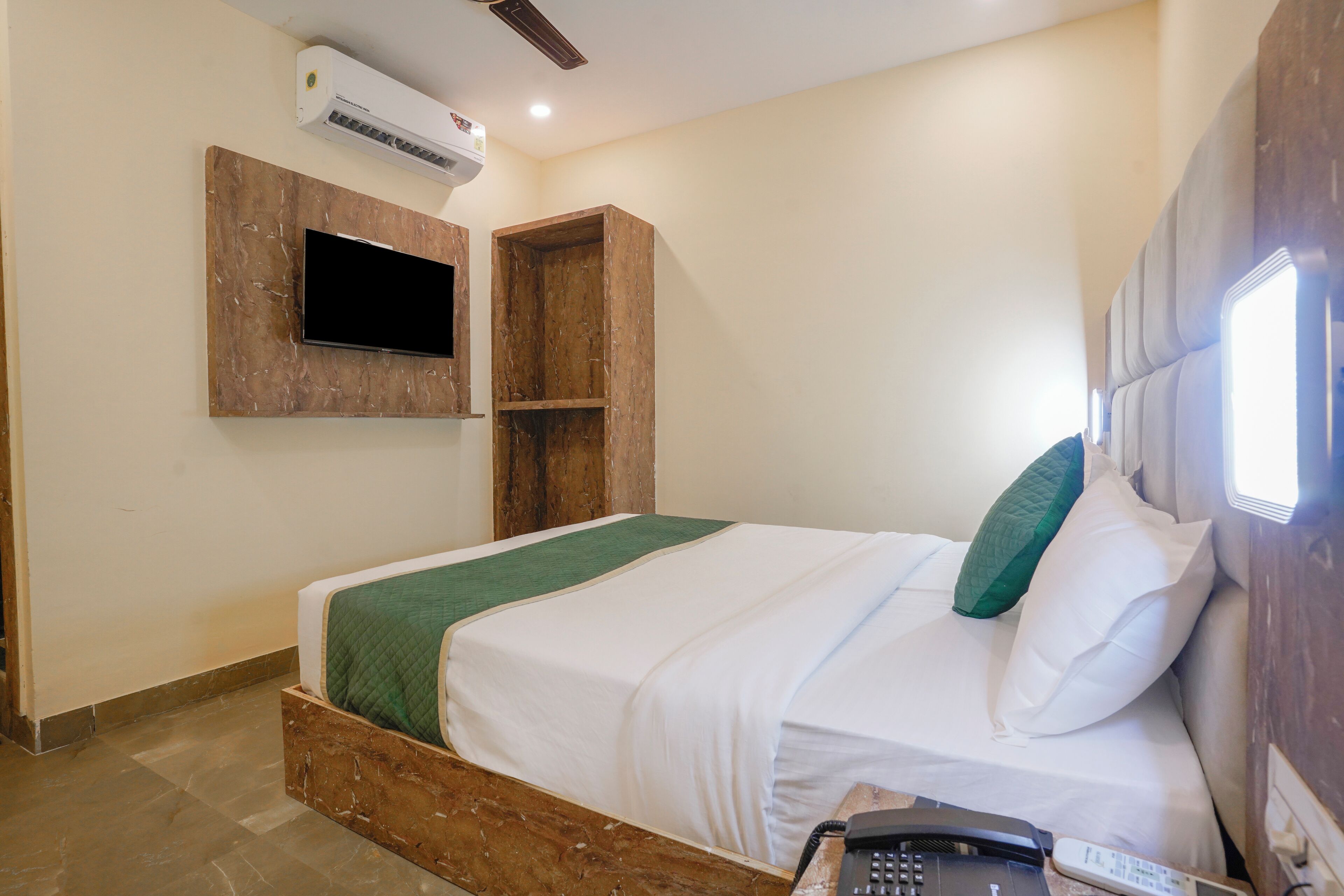 Ein Hotelzimmer mit Bett, Wand-Fernseher, Klimaanlage und Nachttischtelefon.