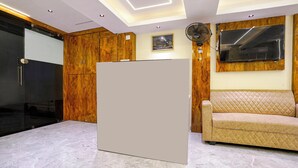 A modern living room with a large white cabinet, a beige sofa, wooden paneling, a mounted TV, and a ceiling fan. - Crystal By Glitz Hotels (Mumbai)