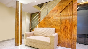 A modern lobby with a beige cushioned sofa, a marble floor, a wooden accent wall, and a staircase with metal railings. - Crystal By Glitz Hotels (Mumbai)