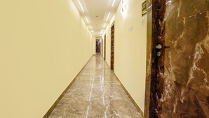 A long, well-lit hallway with marble flooring and walls, leading to a door with a keyhole. - Crystal By Glitz Hotels (Mumbai)