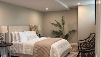 A bedroom with a bed, nightstand, lamp, chair, and a potted plant.