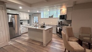 Una cocina moderna con una isla central, electrodomésticos de acero inoxidable y un comedor con mesa y sillas de vidrio.