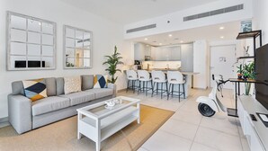 Una sala moderna con un sofá, una mesa de centro y una zona de cocina con taburetes de bar.