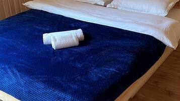 A wooden bed with white bedding and a blue blanket in a room with wooden walls and flooring.