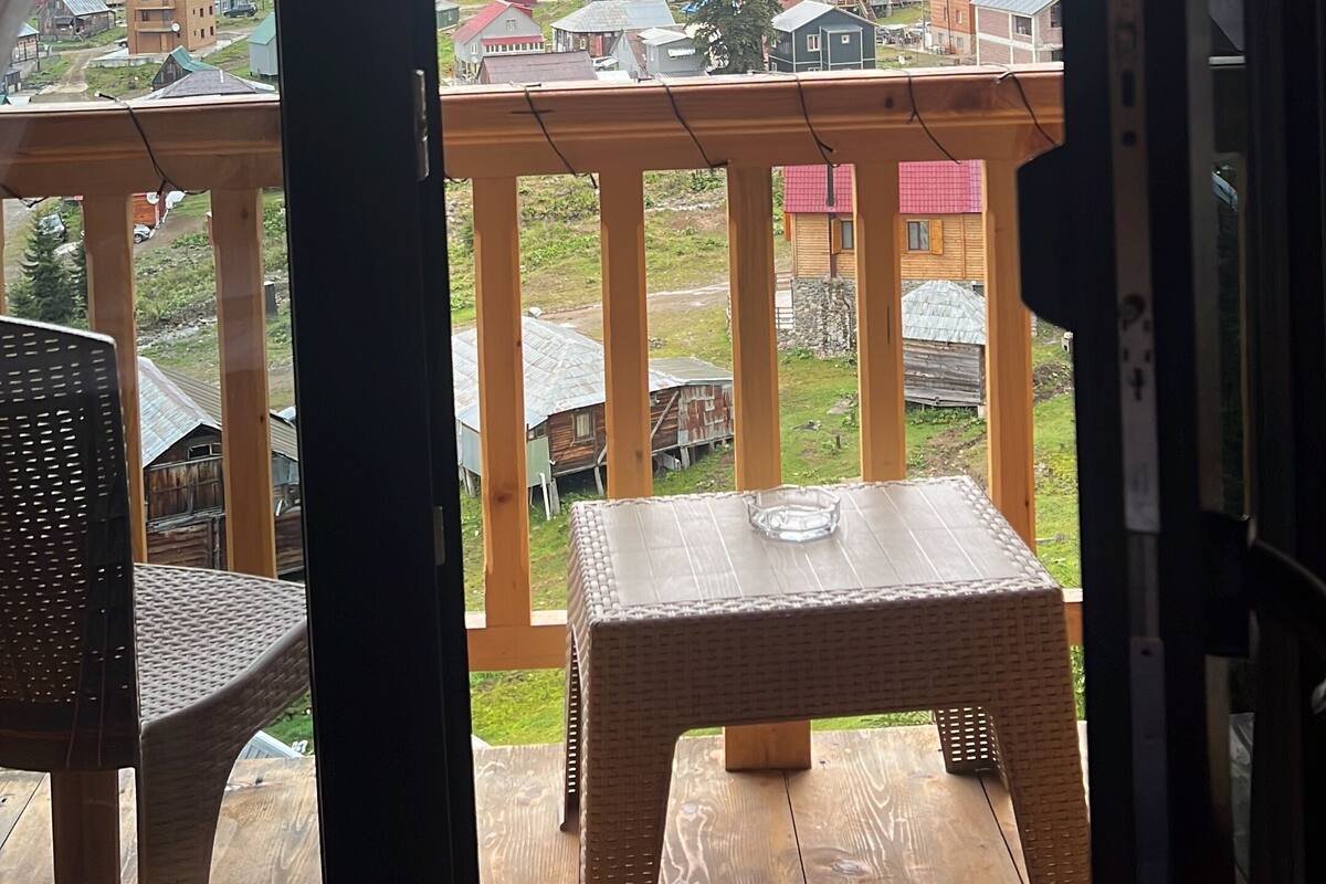 A wooden deck with a table and chairs, overlooking a village with houses and greenery.