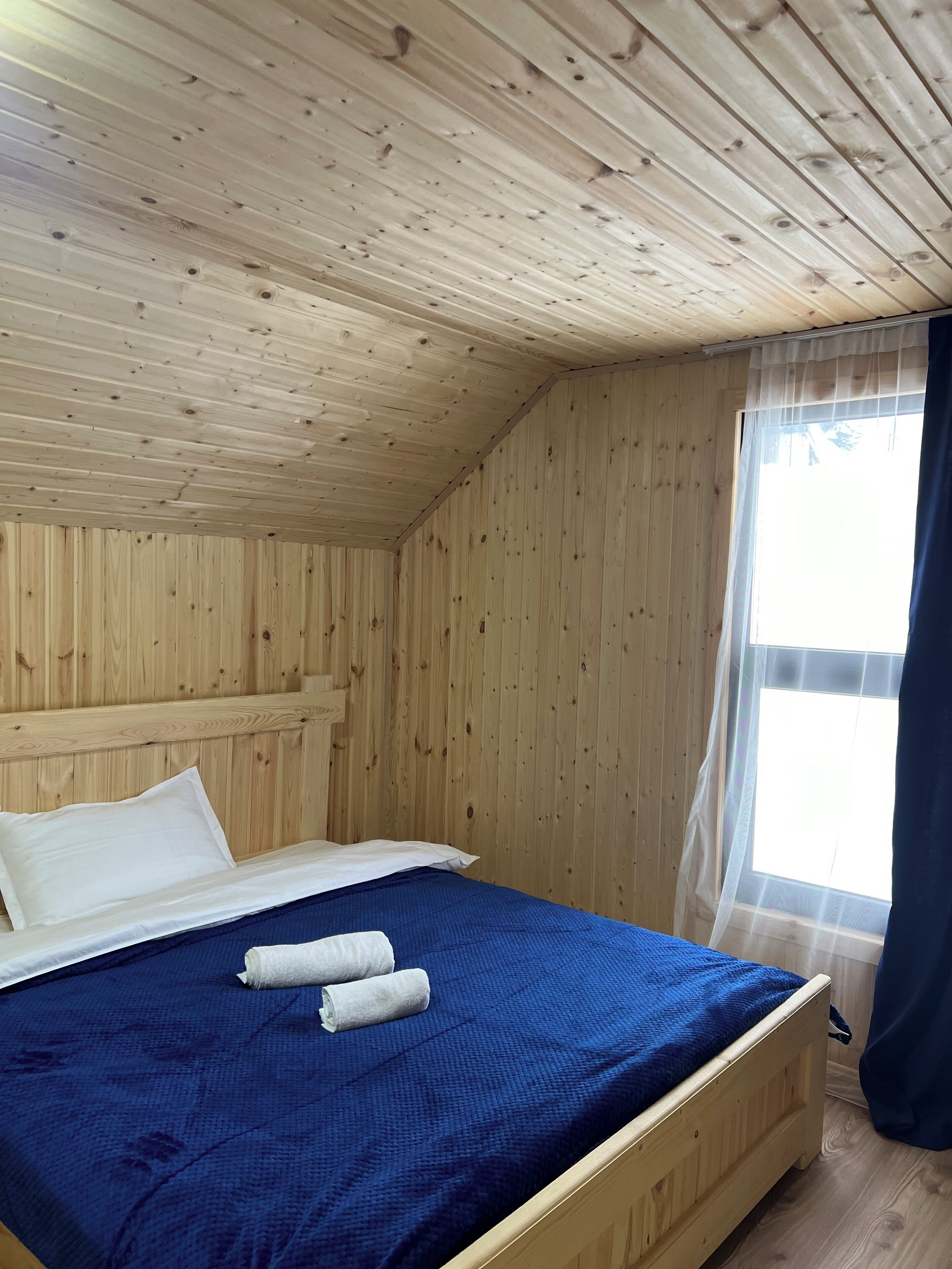 Una stanza con rivestimenti in legno, un letto, una finestra con tende leggere e vista sull'esterno.