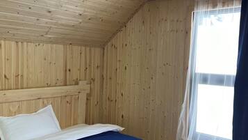Una stanza con rivestimenti in legno, un letto, una finestra con tende leggere e vista sull'esterno.