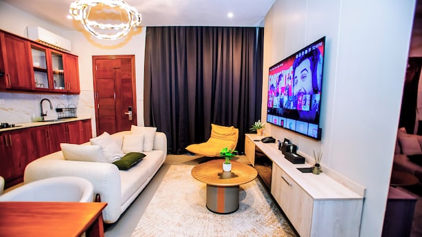 A modern living room with a sofa, coffee table, and a TV mounted on the wall displaying a video game. - Goba Peaks (Dar es Salaam)