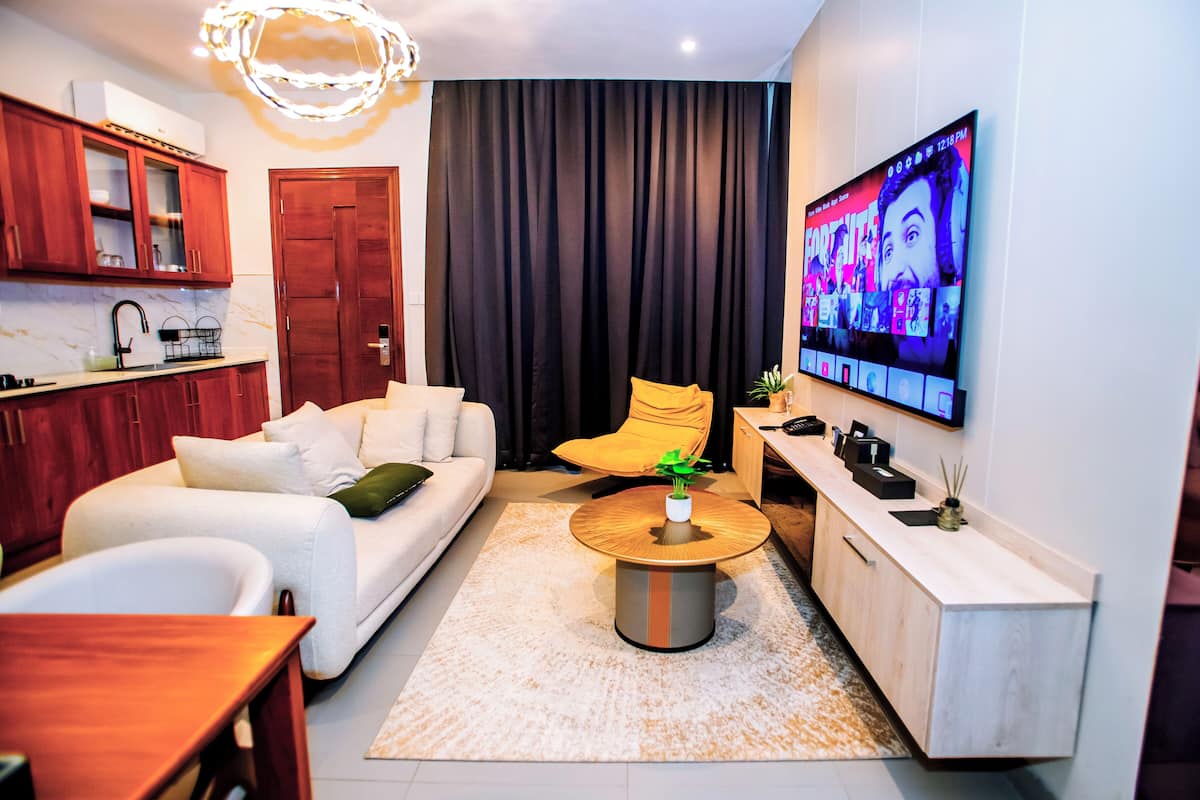 Un salon moderne avec un canapé, une table basse et un téléviseur fixé au mur, sur lequel est affiché un jeu vidéo.