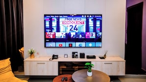 A modern living room with a flat-screen TV mounted on the wall displaying a news channel. - Goba Peaks (Dar es Salaam)