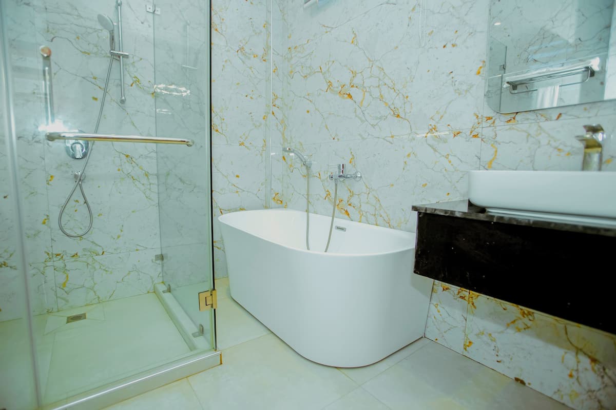Une salle de bain moderne dotée d’une douche à parois de verre, d’une baignoire sur pieds et d’un mur recouvert de carreaux de marbre.