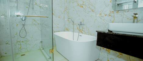 A modern bathroom with a glass-enclosed shower, a freestanding bathtub, and a marble-tiled wall.