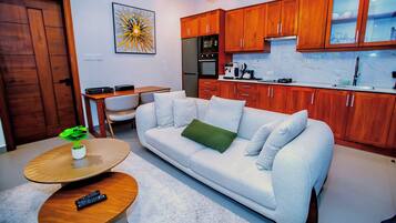 Una sala de estar moderna con un sofá, una mesa de centro y una cocina con armarios de madera y electrodomésticos.